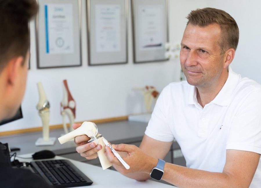 Kniesprechstunde, Prof. Philipp Niemeyer von der OCM Orthopädische Chirurgie München mit jungem Patienten, rechte Hand hält Kniemodell