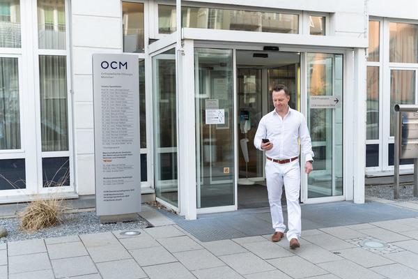 Arzt in weißer Kleidung vor der Eingangstür der OCM Praxis und Klinik