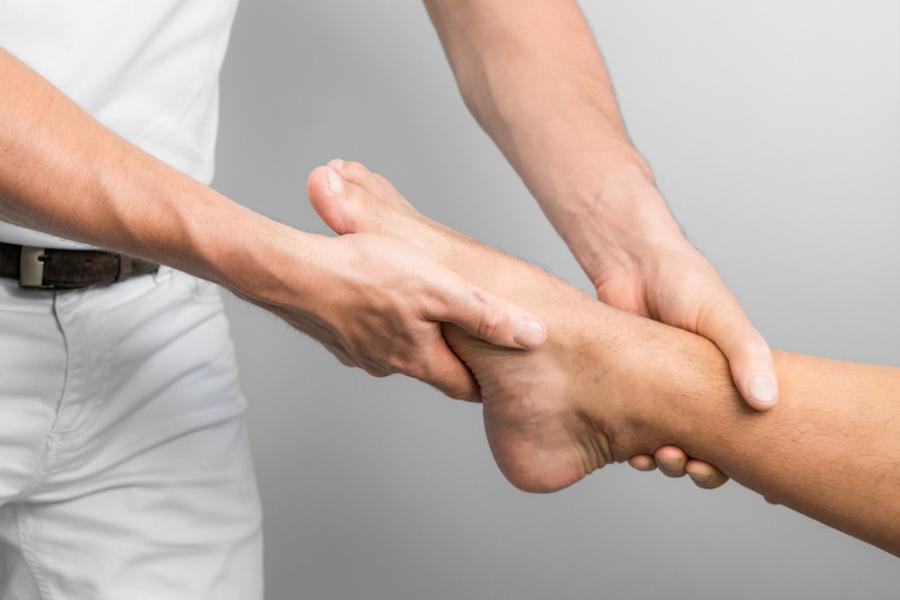 Großaufnahme eines menschlichen Fußes, beide Hände eines Arztes untersuchen den Fuß