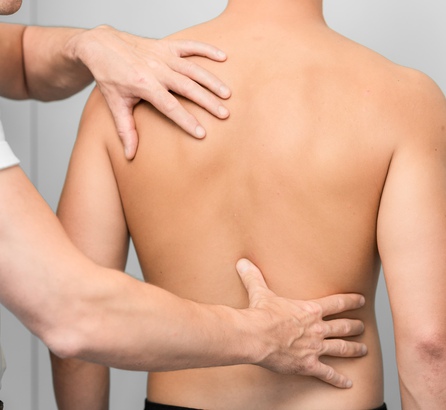 Arzt untersucht mit beiden Händen den unbekleideten Rücken eines jungen Mannes