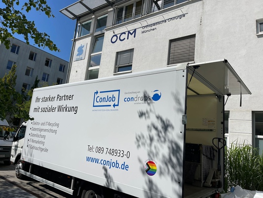 Seitenansicht eines weißen Lkw vor der OCM Praxis in München, die Sonne scheint.