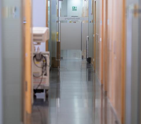 Blick auf die Türen der Behandlungsräume der OCM Orthopädische Chirurgie München, schmaler Gang, am Ende eine Glastür