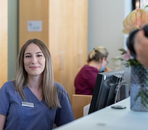 Young female employee, smiling, seated at the reception desk of the OCM München