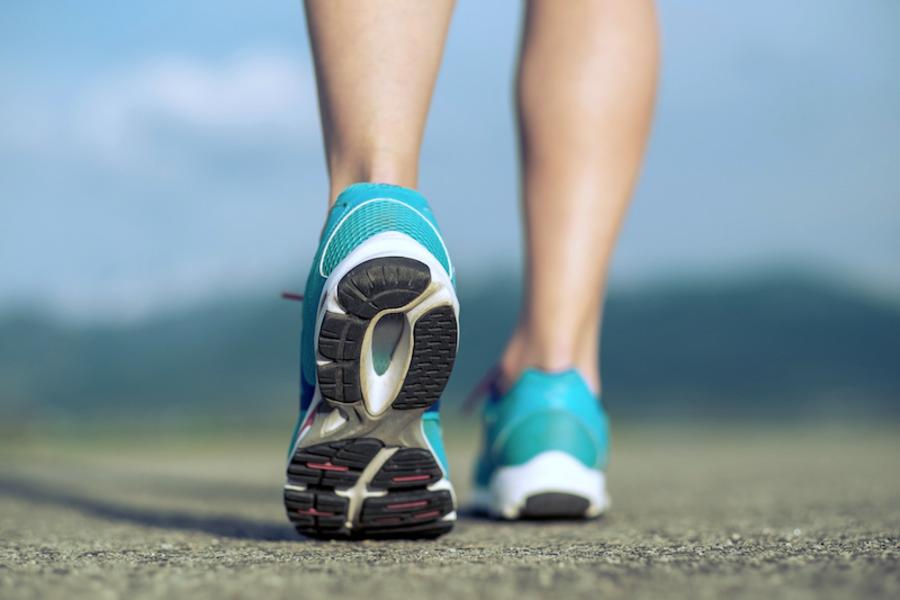 Großaufnahme Beine einer Läuferin von hinten, Sportschuhe, Achillessehnen sichtbar, linker Fuß hebt vom Boden ab, linke Ferse ohne Bodenkontakt