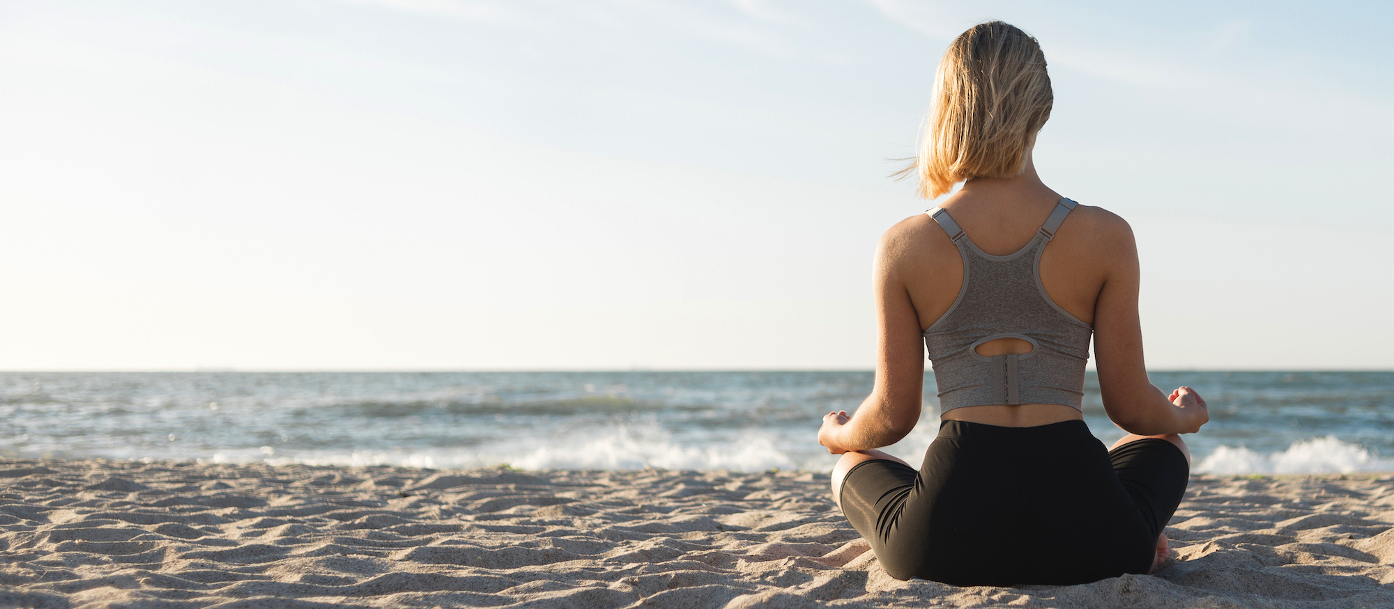 Frau, von hinten zu sehen, sitzt in Yoga-Position am Strand